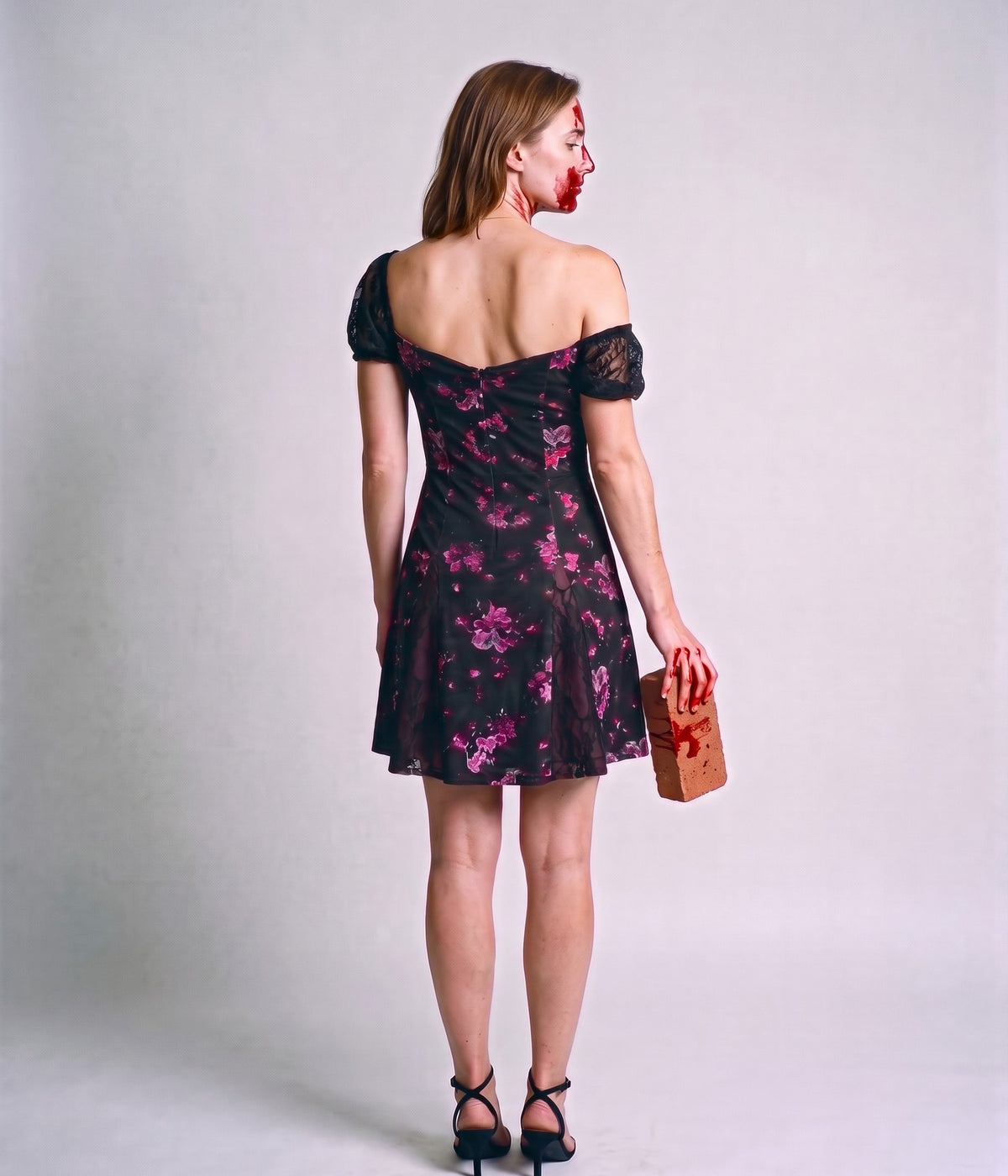 Back view of the floral mini dress with lace puff sleeves, the model holding a brick along her leg on a grey background
