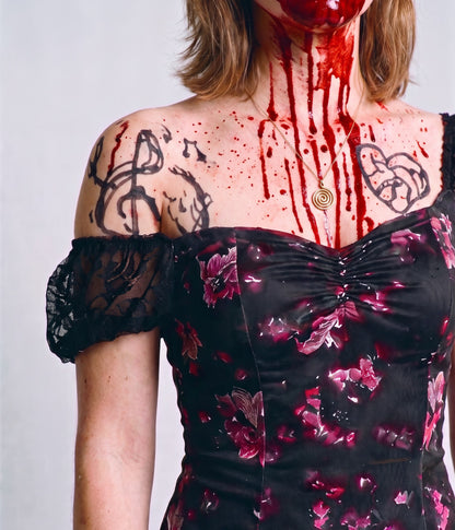 Close-up of the floral mini dress neckline with a lace puff sleeve, black marker tattoos and fake blood makeup on the chest